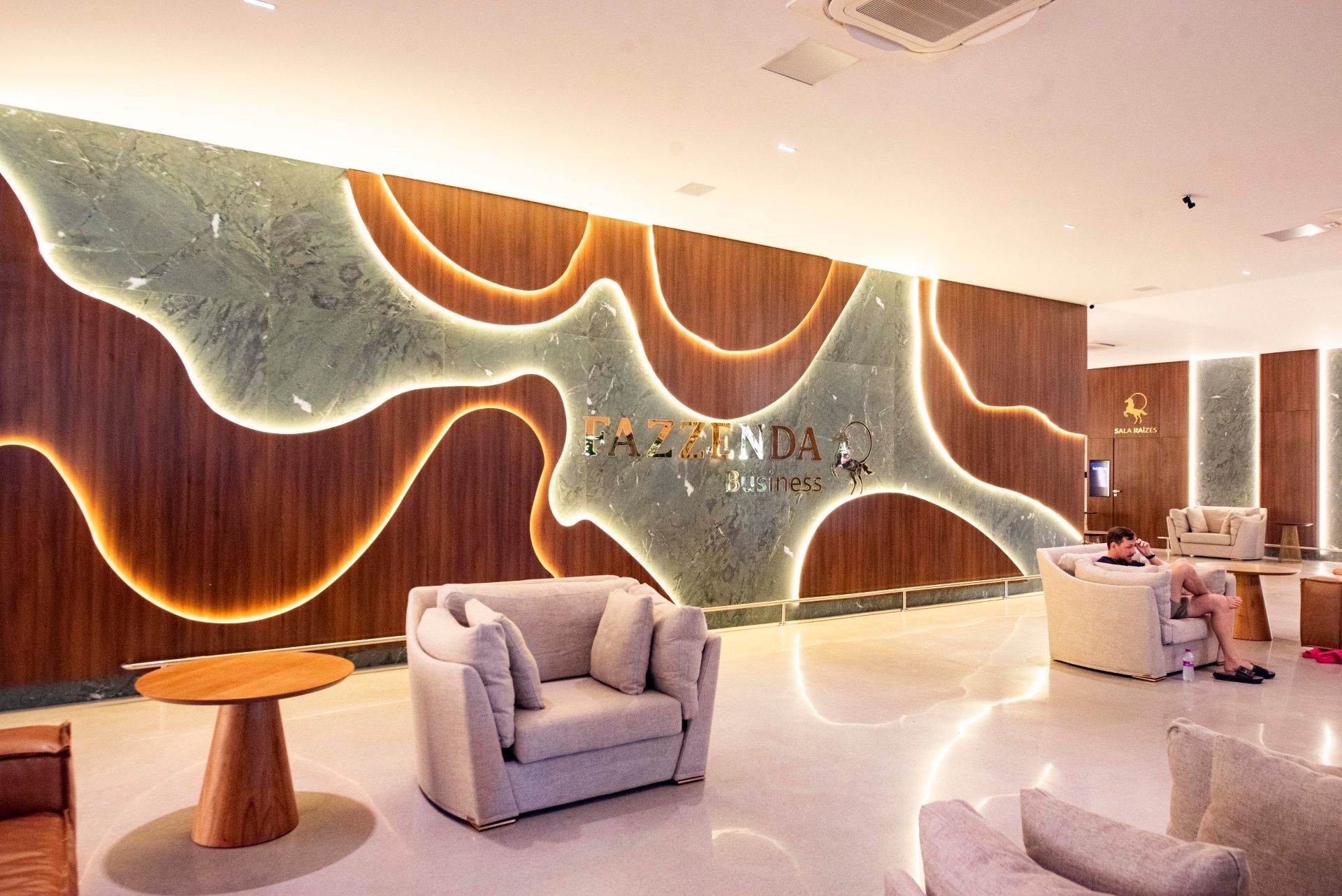 Sala de estar moderna com obras de arte esculturais na parede, iluminação aconchegante e cadeiras cinza-claro em um lobby elegante.