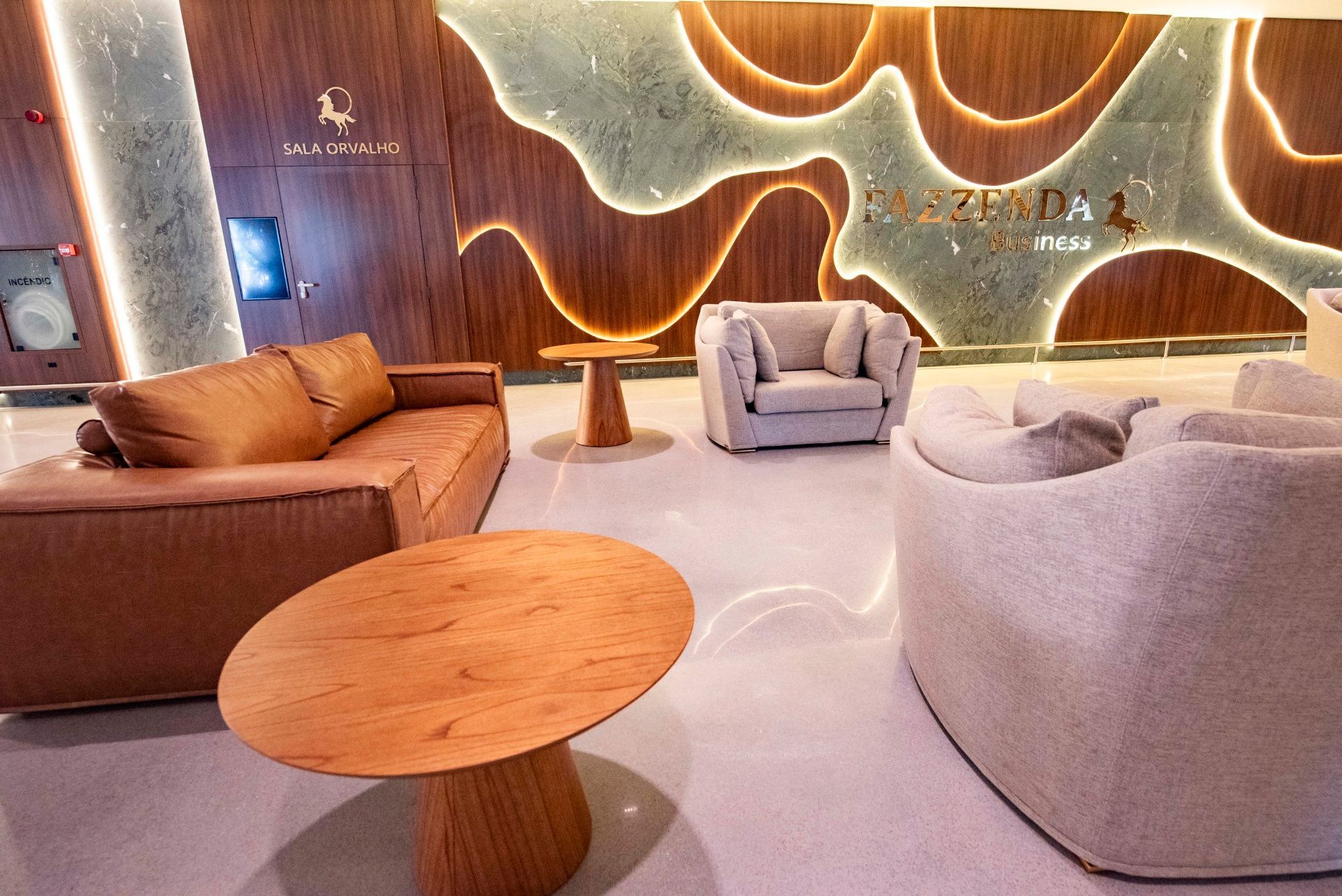 Sala de estar moderna com sofás curvos, mesas redondas de madeira e uma parede com iluminação aconchegante.