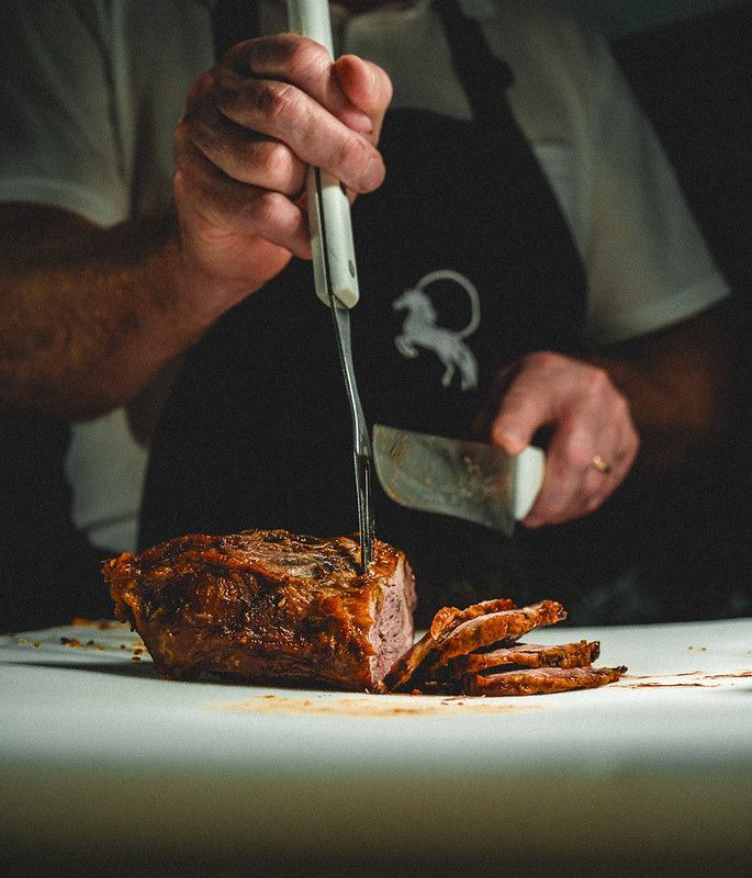 Pessoa fatiando um prato de carne assada com uma faca em um prato na cozinha.
