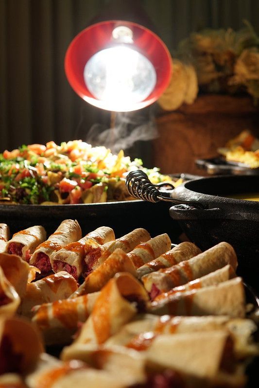 Buffet com doces, saladas e um aquecedor aceso em uma mesa de serviço com iluminação suave.