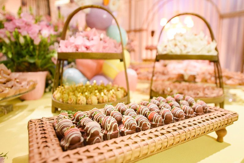 Trufas de chocolate sortidas em uma bandeja de vime em um bufê de sobremesas em tons pastel.