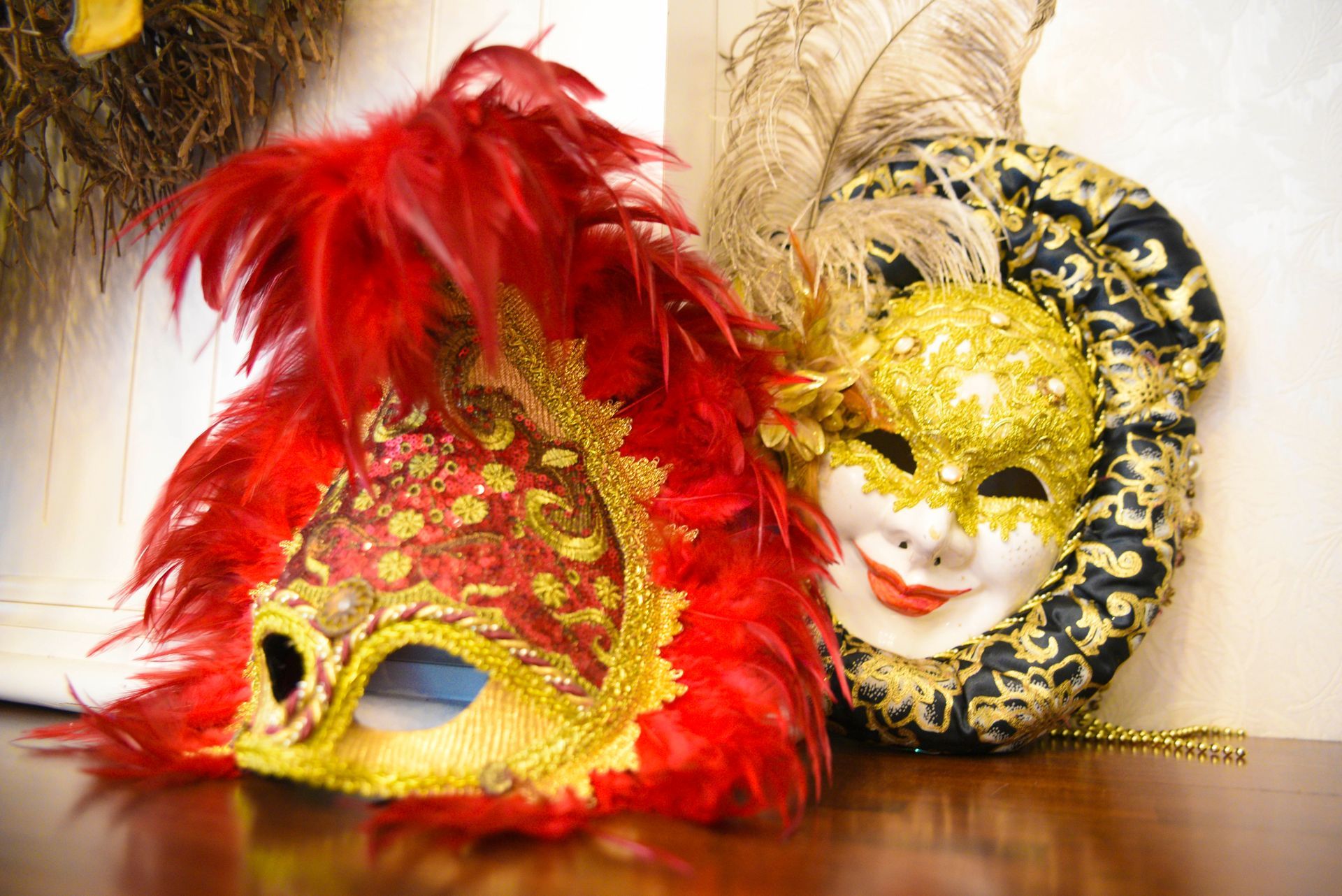 Duas máscaras venezianas ornamentadas, uma vermelha com penas e outra dourada com renda preta, repousam sobre uma mesa.