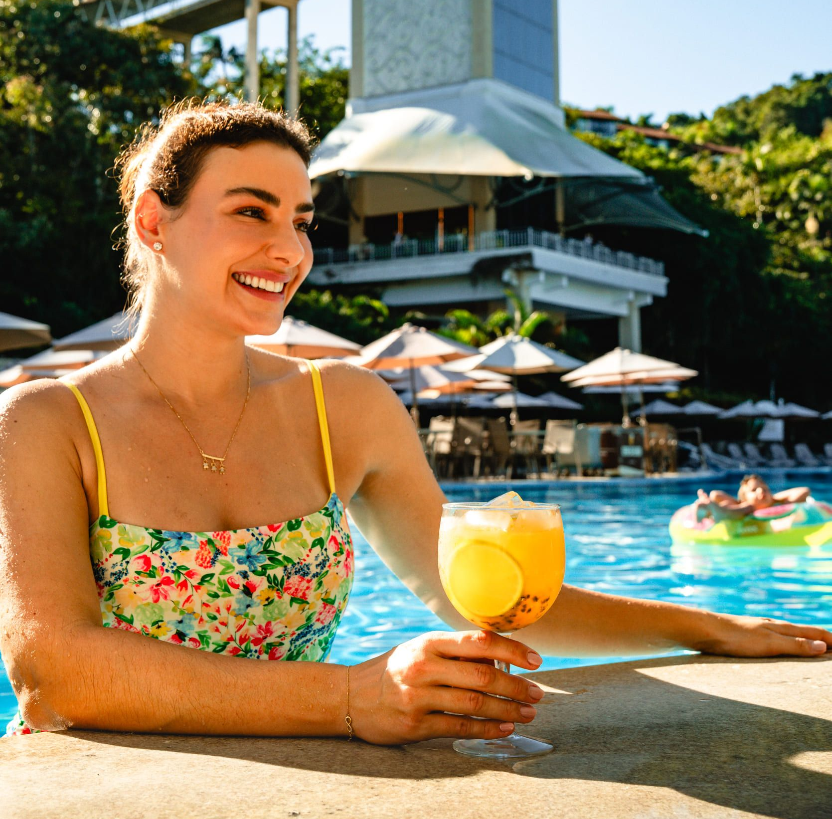 Bebida de frutas tropicais com kiwi e cereja como guarnição, servida em um copo transparente à beira da piscina.