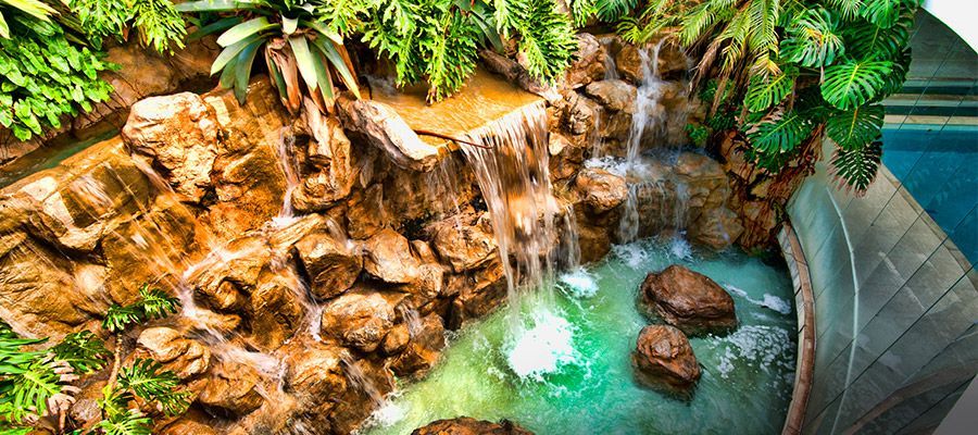 Cachoeira tropical que deságua em uma piscina turquesa ao lado de paredes rochosas e plantas verdejantes.