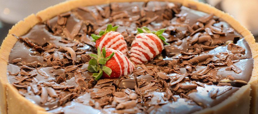 Bolo de chocolate coberto com raspas de chocolate e dois morangos no centro.