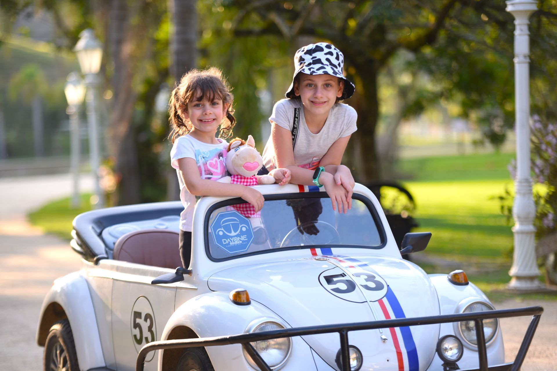 Criança sentada em um carro de corrida branco, número 53, sorrindo ao volante.