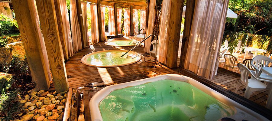 Deck de spa rústico com uma pequena banheira de hidromassagem redonda e uma piscina rebaixada sob colunas de madeira.