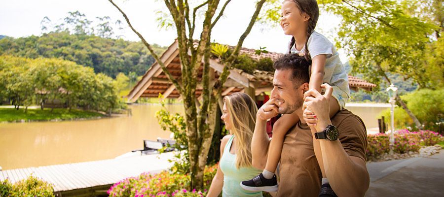 Família aproveitando um passeio de cavalinho à beira de um lago, com um pavilhão de madeira e vegetação exuberante ao fundo.
