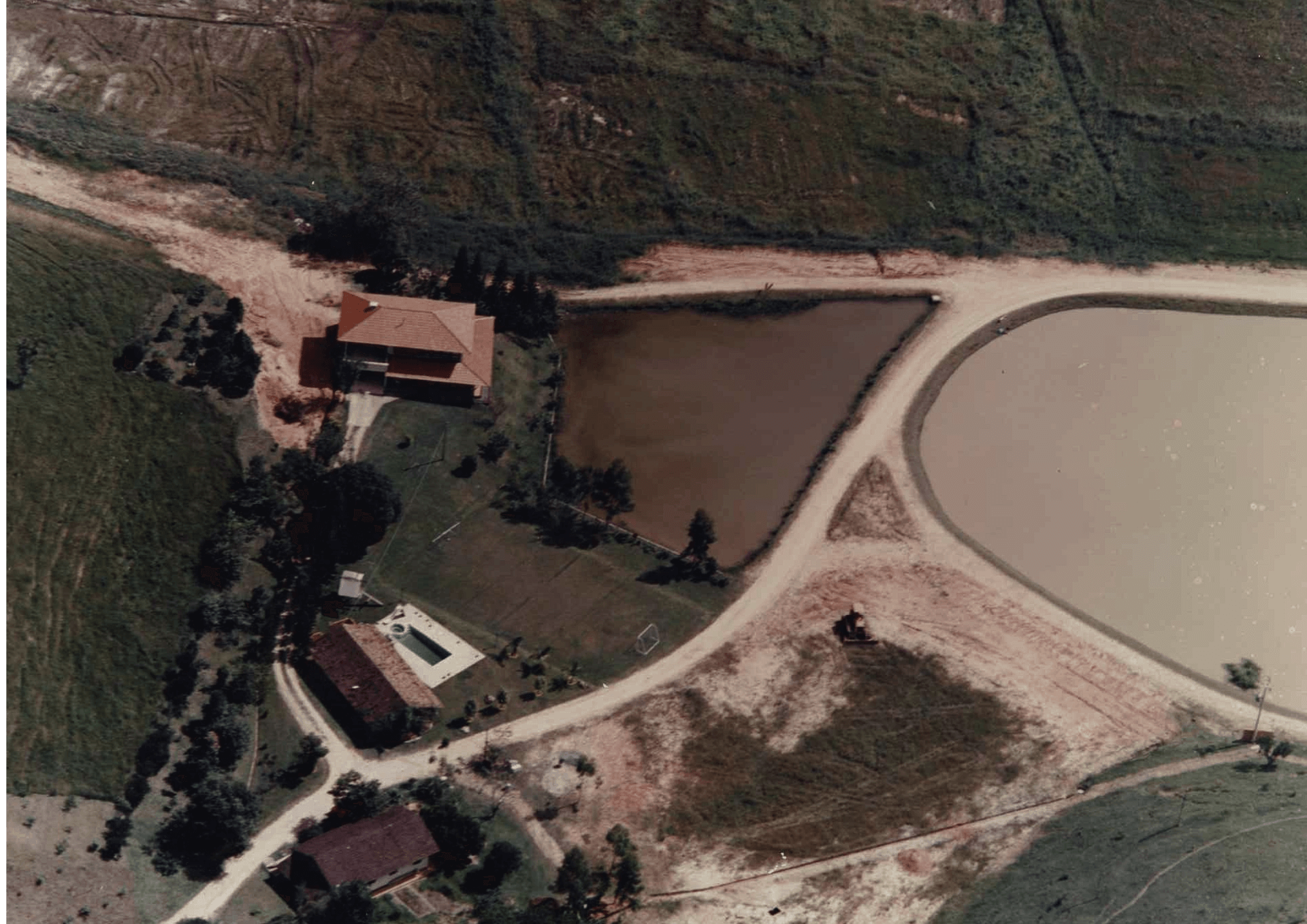 Vista aérea de uma fazenda rural com construções, estradas de terra e lagoas ou reservatórios de água.