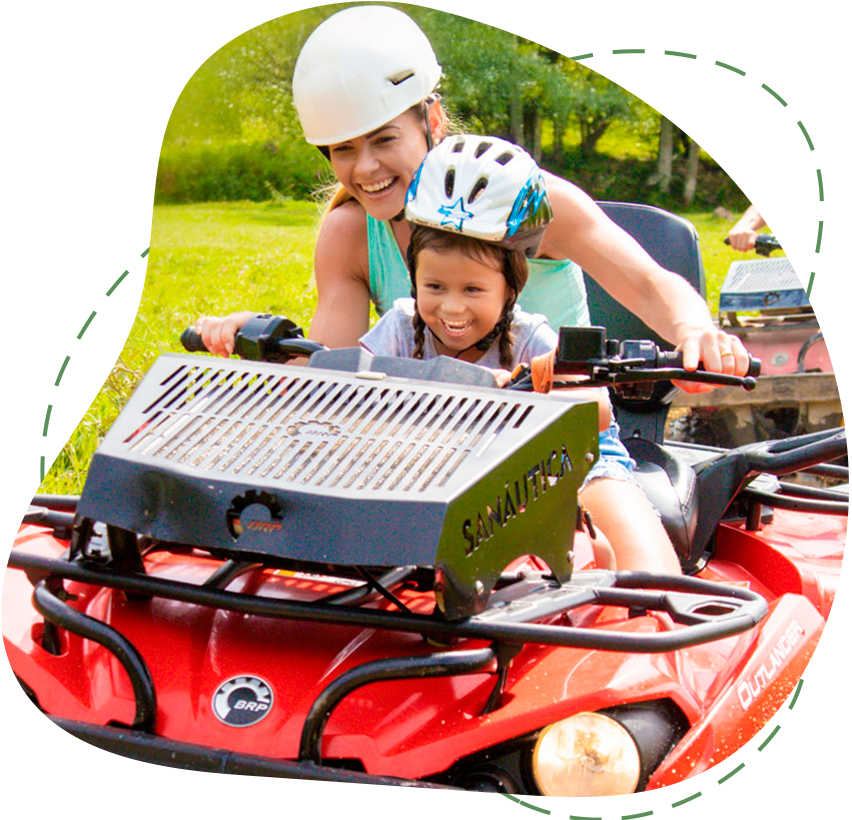 Adulto e criança andando em um veículo off-road vermelho, sorrindo ao ar livre usando capacetes.