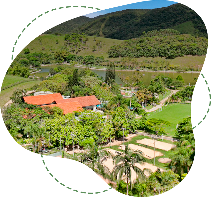 Resort tropical exuberante com edifícios de telhados vermelhos, palmeiras e montanhas ao fundo.