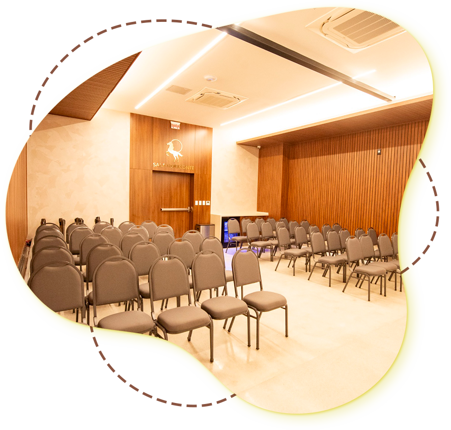 Sala de conferências vazia com fileiras de cadeiras cinzentas, painéis de madeira nas paredes e iluminação embutida brilhante.