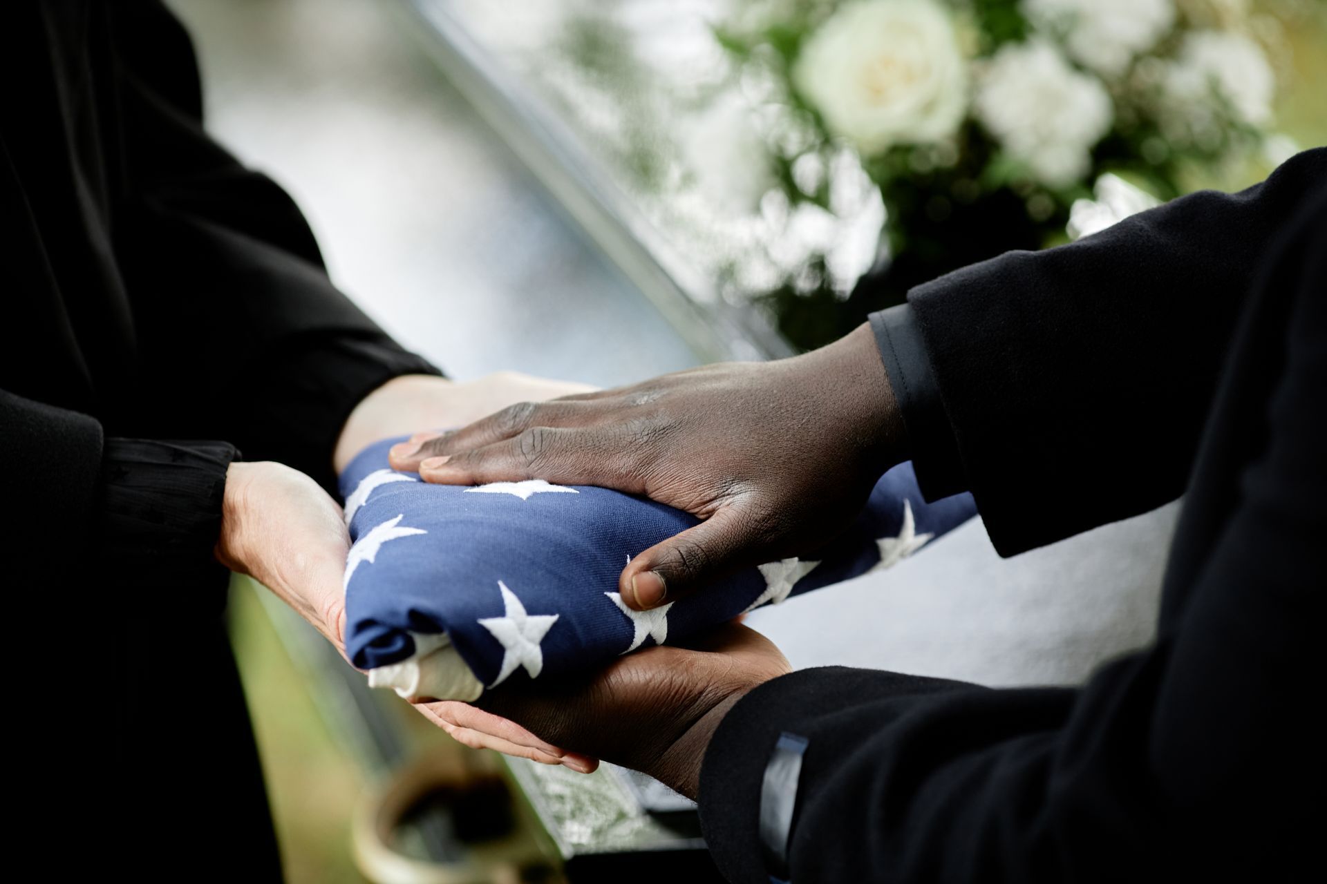 Hands holding folded American flag; funeral ceremony.