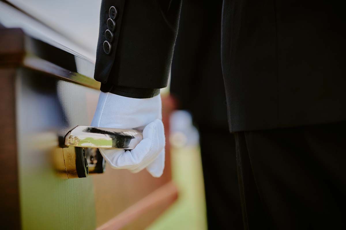 Person in black suit and white glove opens a wooden door with a gold handle.