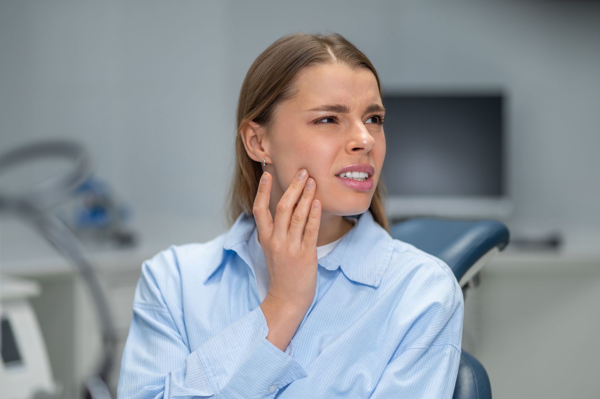 woman sitting in a dental office, touching her cheek with a concerned expression.
