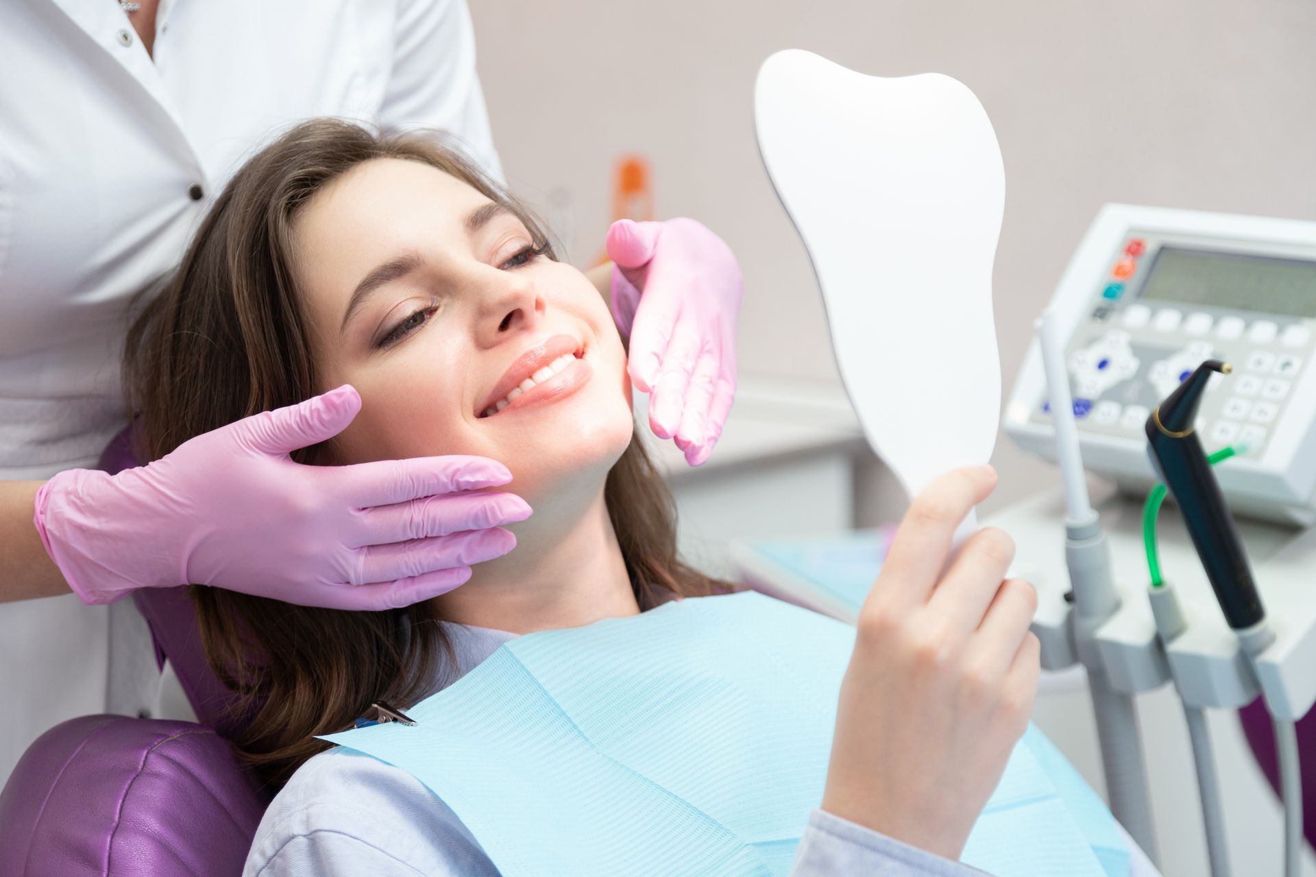 Young smiling woman patient looking at mirror after teeth whitening procedure.