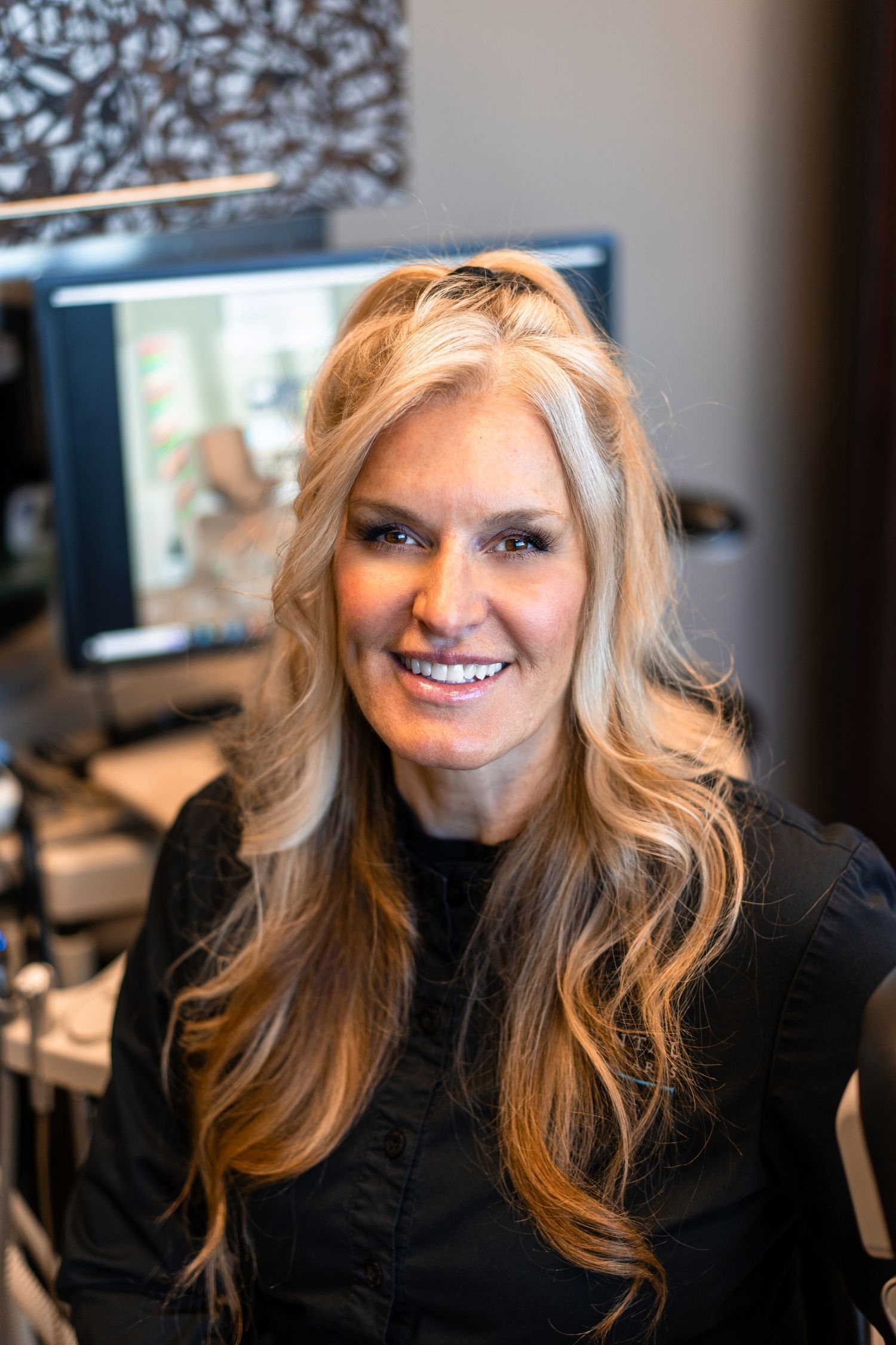 Smiling woman in a black top seated at a desk with a computer monitor in the background