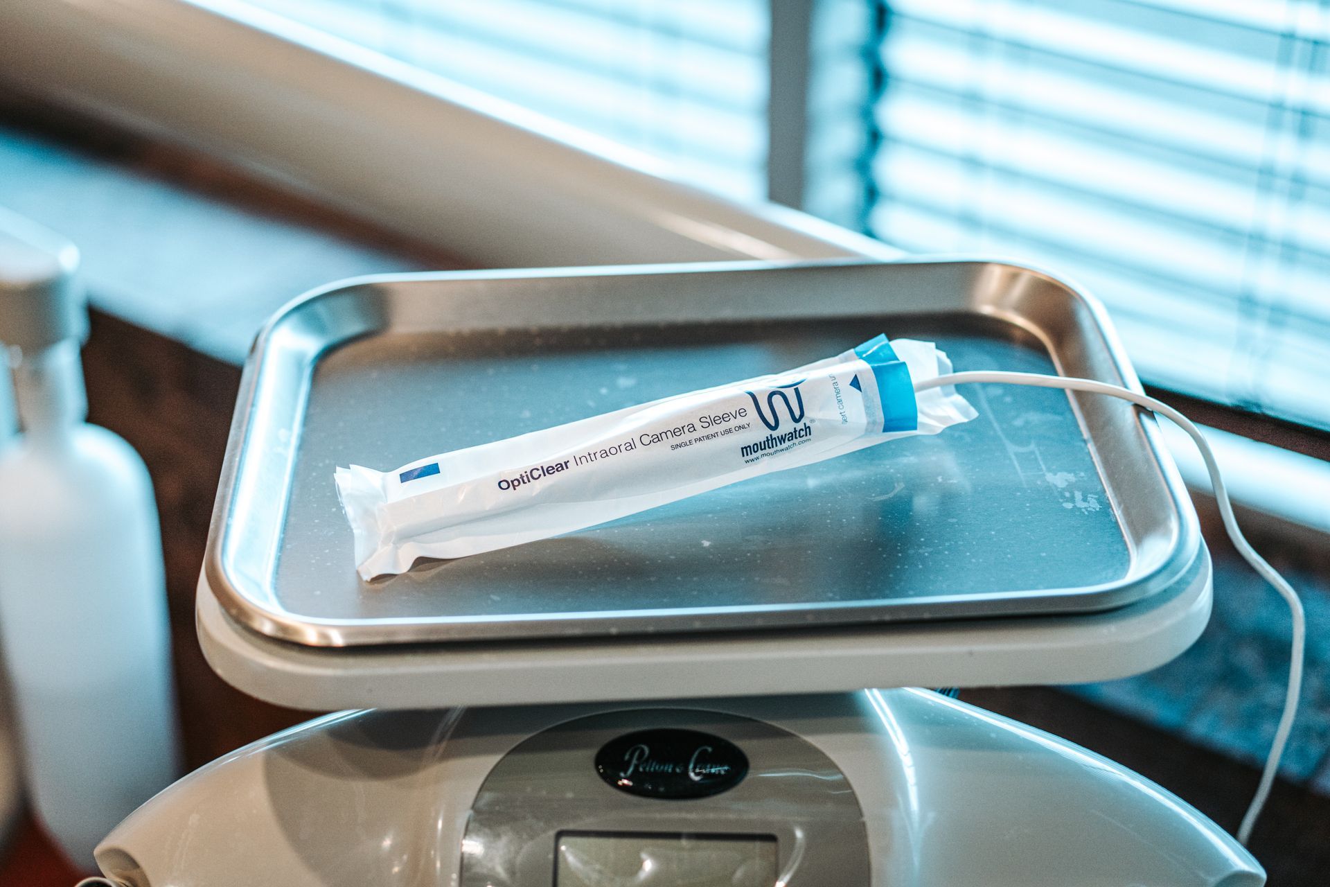 A sterile-packaged medical sensor with a white cable rests on a metal dental tray atop a clinical station.