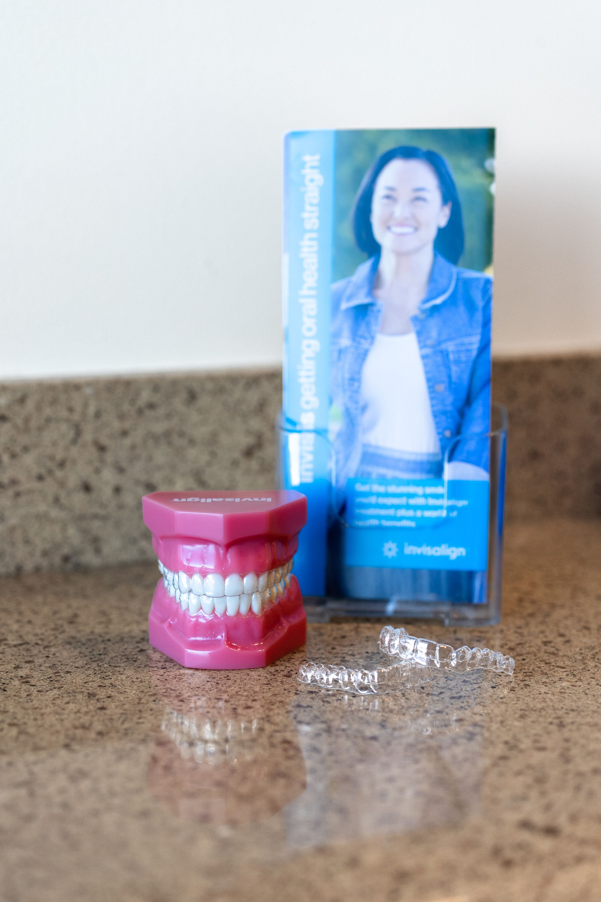 Model of teeth with braces, Invisalign tray, and promotional material on a counter.