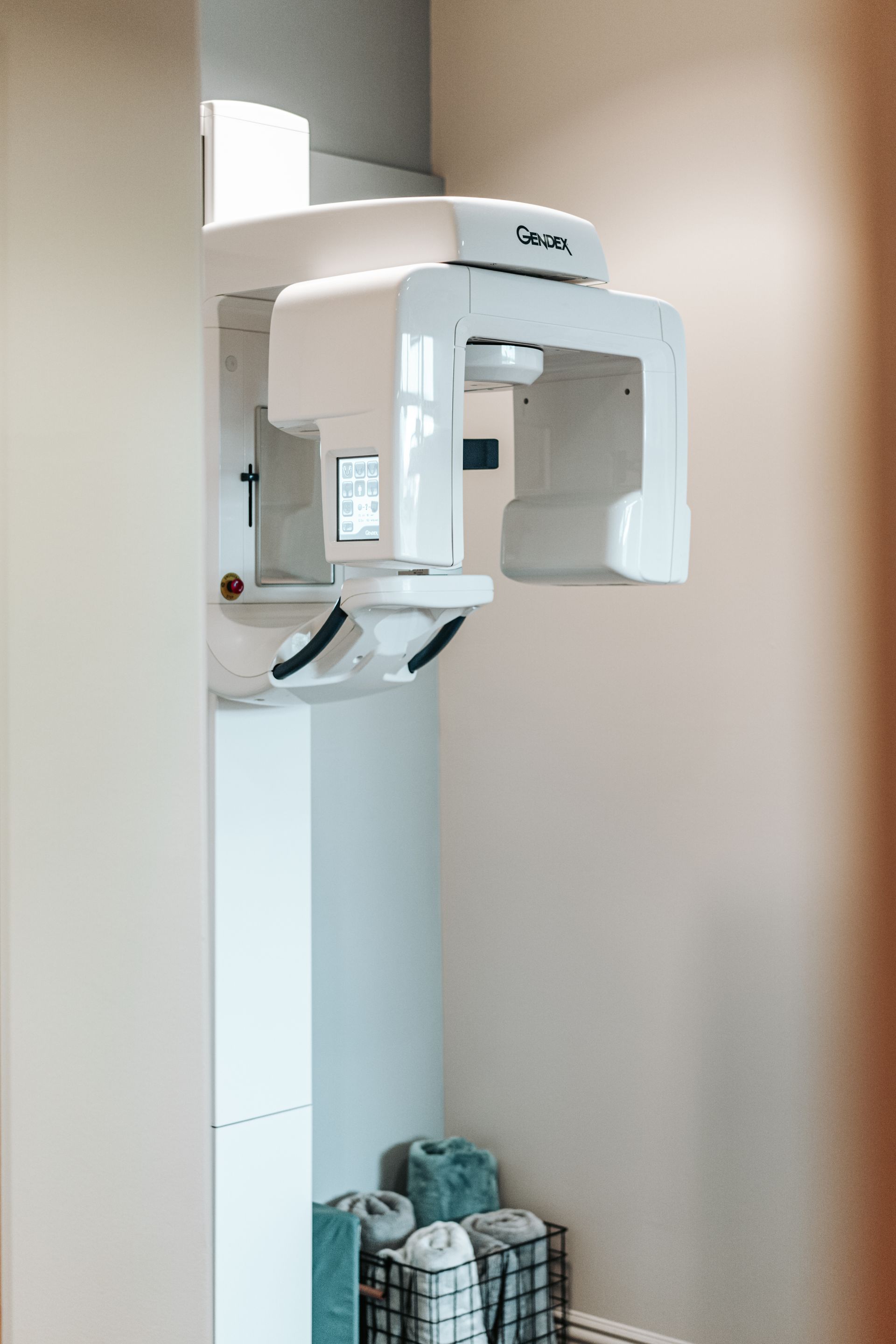 A white dental panoramic X-ray machine mounted on a wall in a clinical office setting.