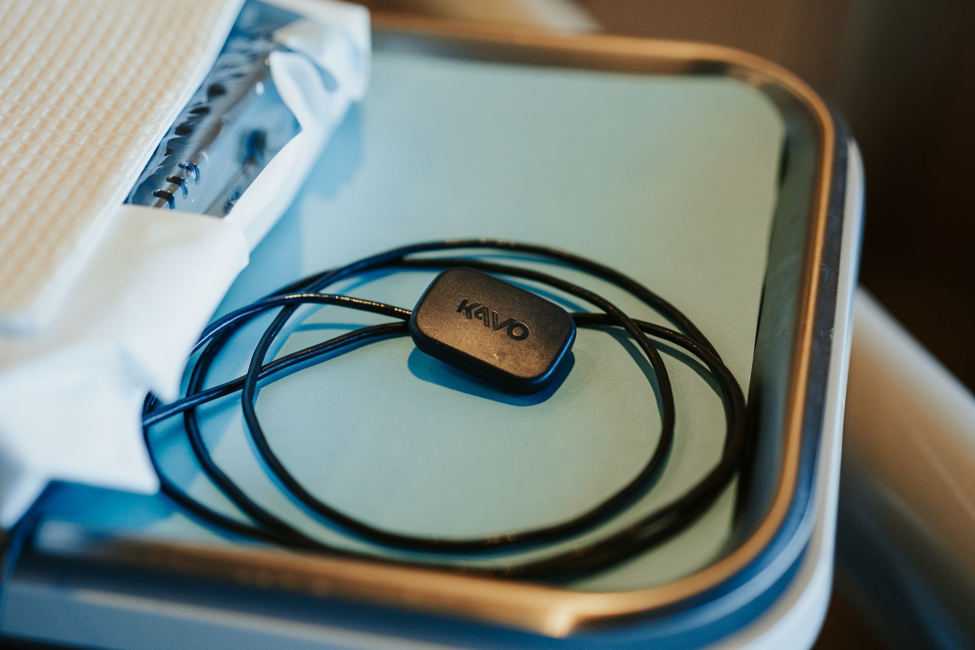 A black digital sensor with a coiled wire rests on a smooth, light blue tray.