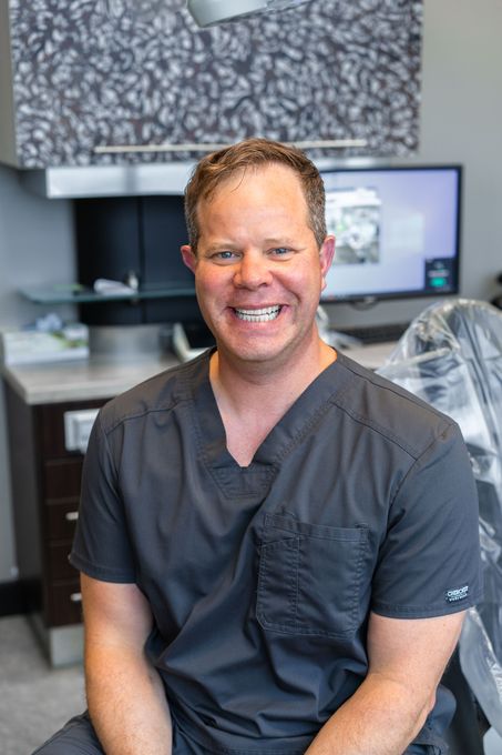 Man smiling in a dental office setting, wearing scrubs.