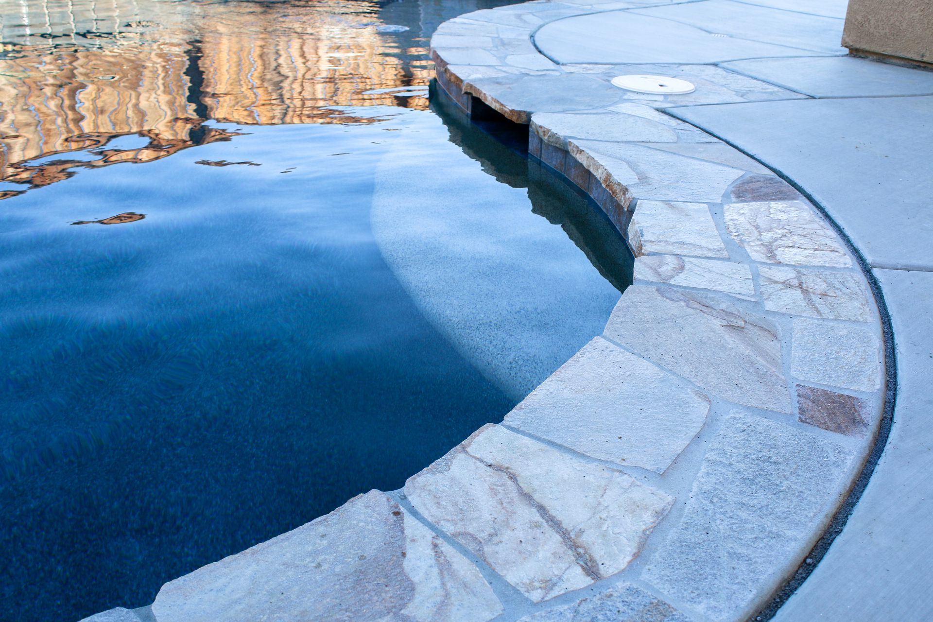 A stone-edged swimming pool deck curving along the edge of dark blue water.