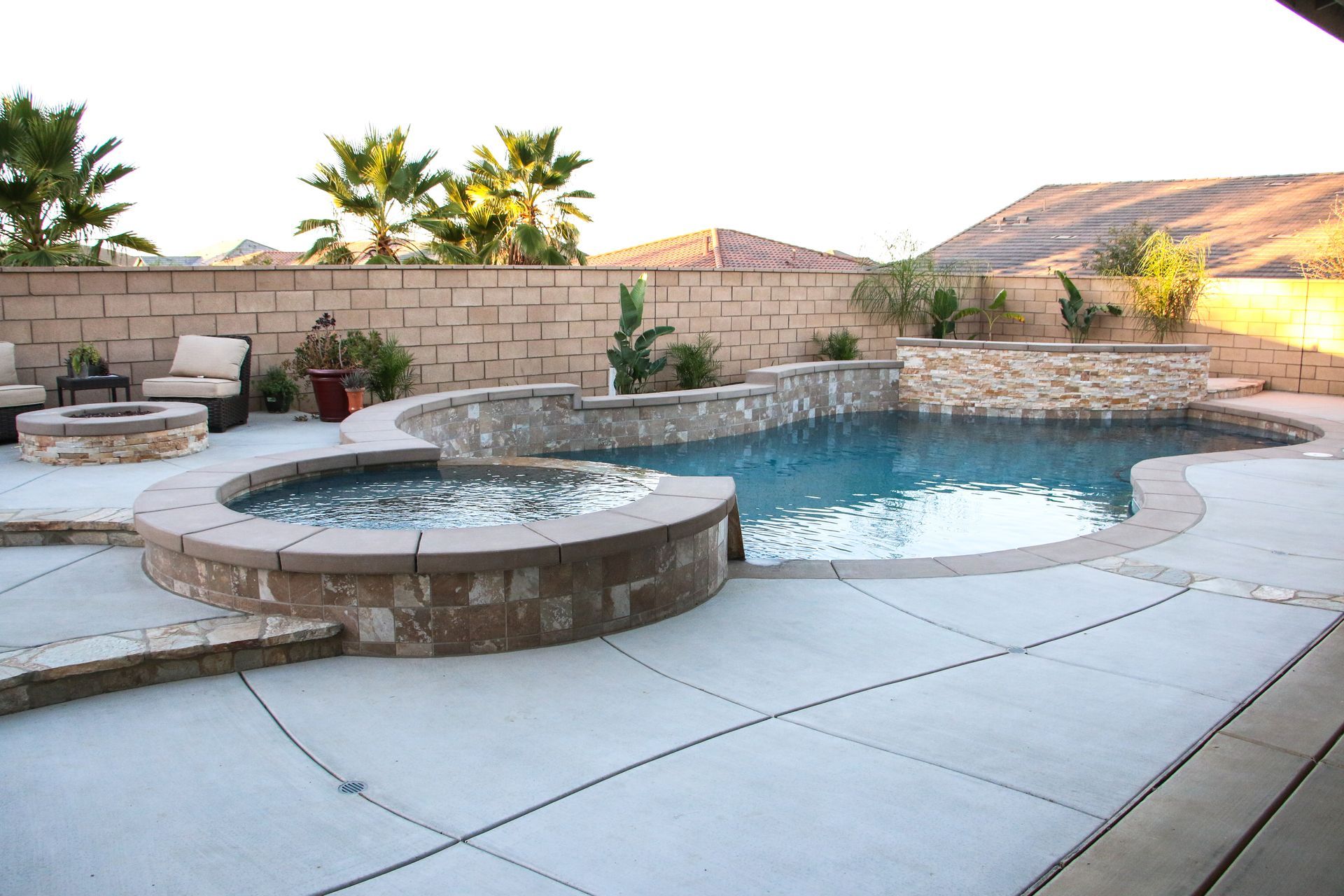 A backyard swimming pool and raised hot tub with stone accents, lounge chairs, and a desert mountain view.