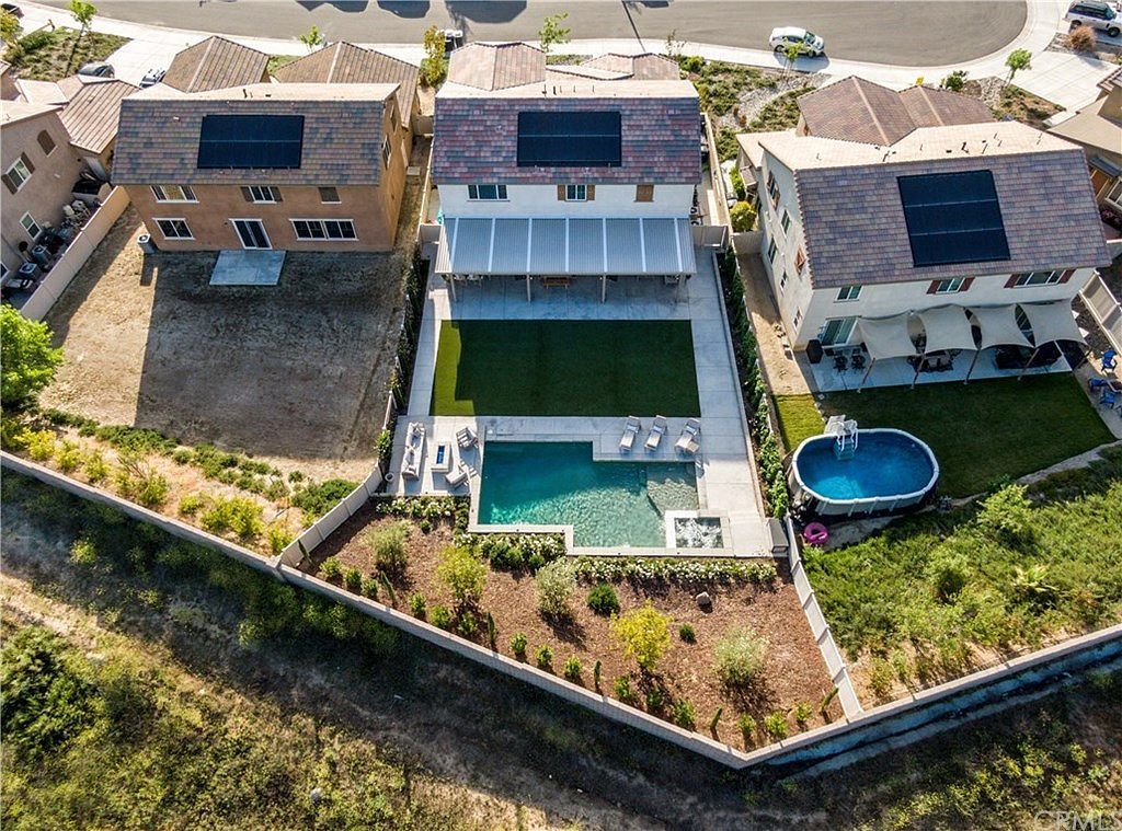 An aerial view of three residential homes with solar panels and backyards.