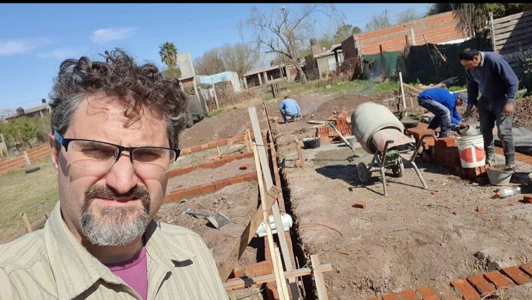 Hombre tomándose un selfie con trabajadores de la construcción que construyen un muro de ladrillos al aire libre.