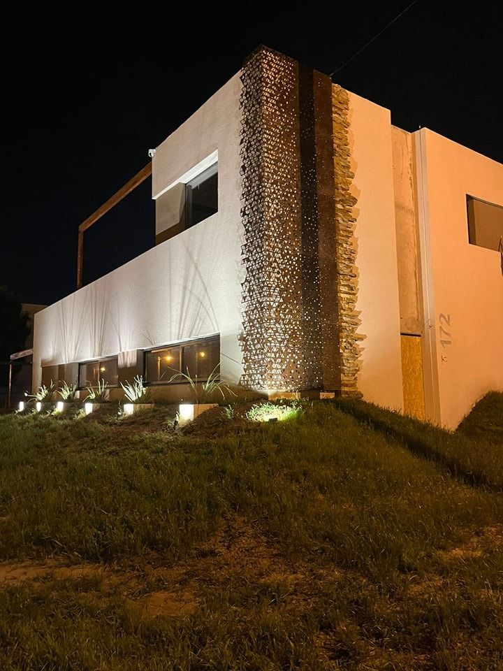 Edificio moderno de noche con pared de acento de piedra y patio ajardinado.