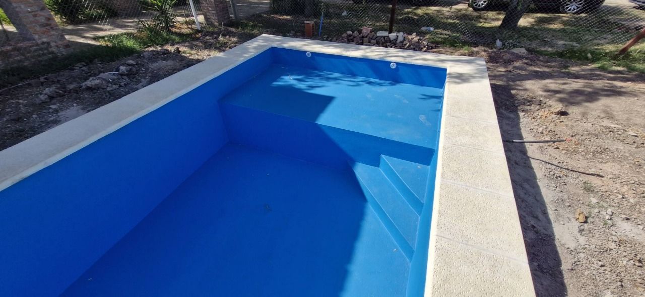 Una piscina azul con escalones y borde de hormigón blanco. Al aire libre.
