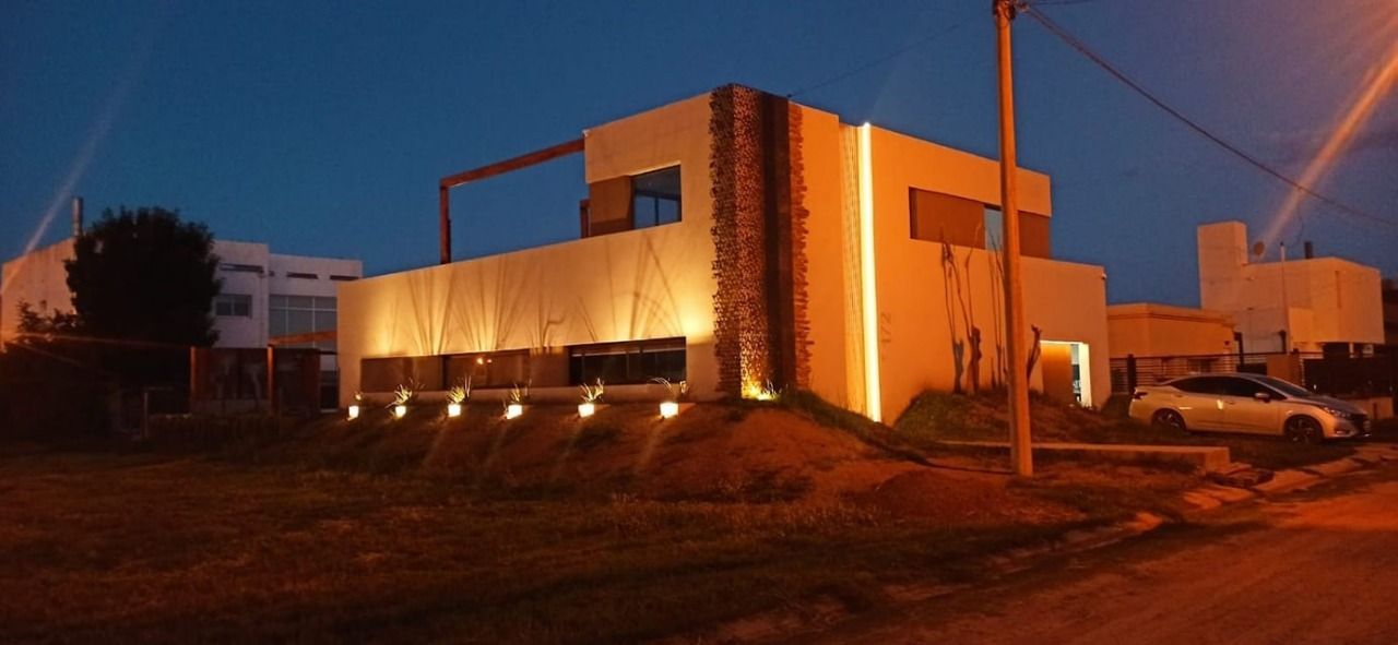 Exterior de una casa moderna al anochecer, con elementos iluminados. Hay un coche aparcado en la entrada.