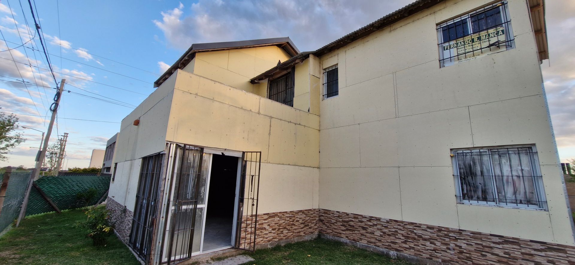 Casa beige de dos plantas con rejas en las ventanas. Puerta de piedra marrón y madera. Cielo nublado.