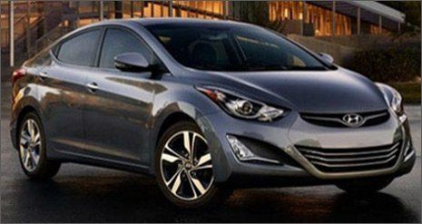 Un sedán Hyundai gris estacionado al aire libre al atardecer frente a un edificio moderno.