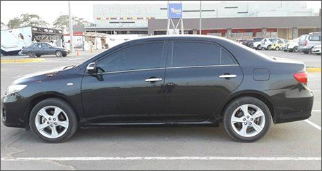 Sedán negro estacionado en un lote frente a una tienda minorista.