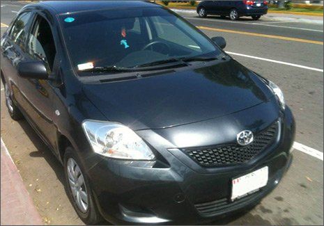 Sedán Toyota negro estacionado al costado de la carretera con pegatinas visibles en el parabrisas