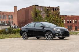 Un sedán negro estacionado frente a un antiguo edificio de ladrillo con hiedra en la pared.