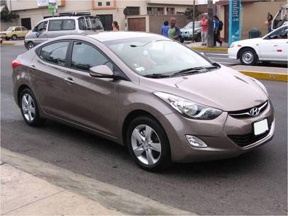 Sedán marrón estacionado en una calle con edificios y peatones al fondo.