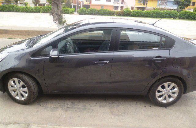 Sedán gris oscuro estacionado en una entrada de vehículos con casas al fondo.
