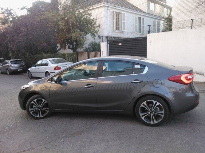 Un sedán gris estacionado en una calle frente a una casa blanca y una pared.
