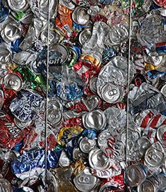 Crushed aluminum soda cans piled in a recycling bin, showing silver, red, blue, and green colors.