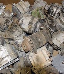 Pile of dusty old metal alternators and generators stacked together in a junkyard.
