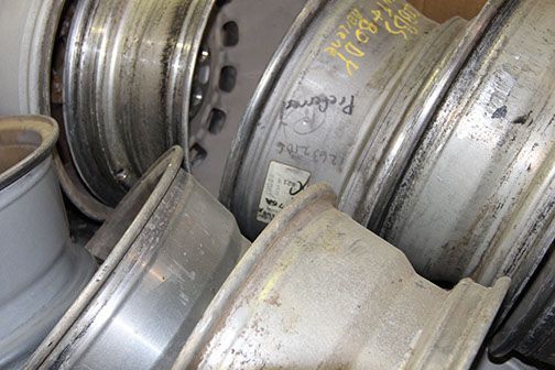 Stacked silver alloy car rims in a pile, with scuffs and yellow chalk markings