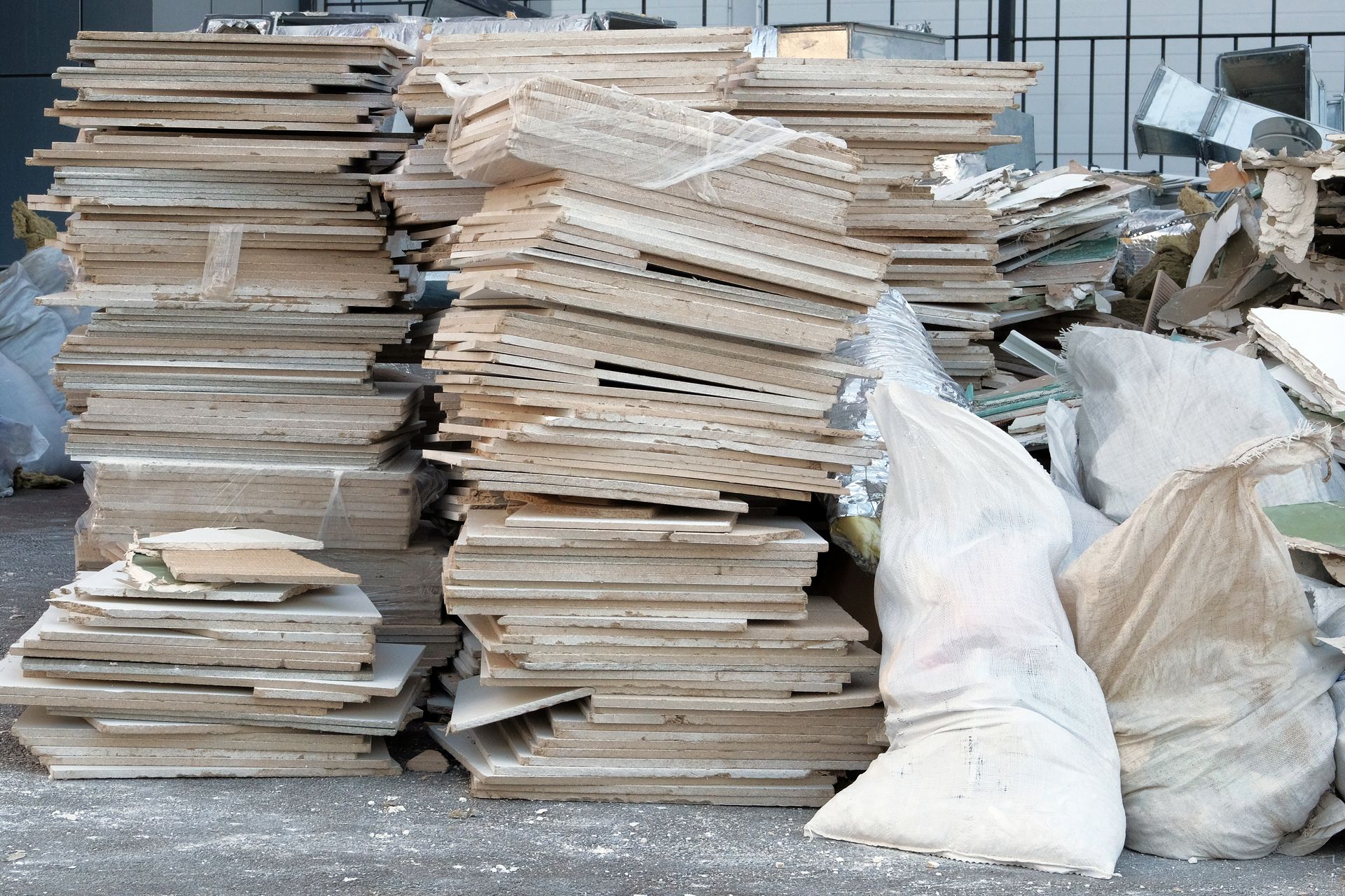 Stacks of cardboard and paper bundles piled outdoors beside white sacks of recyclables.