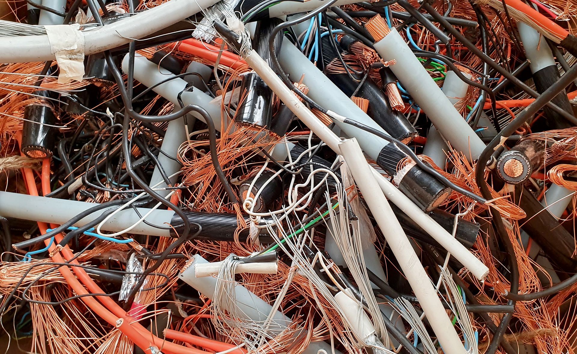 Pile of tangled scrap metal and cables, with orange rust and gray pipes filling the frame
