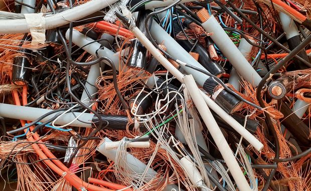 Pile of tangled scrap metal and cables, with orange rust and gray pipes filling the frame
