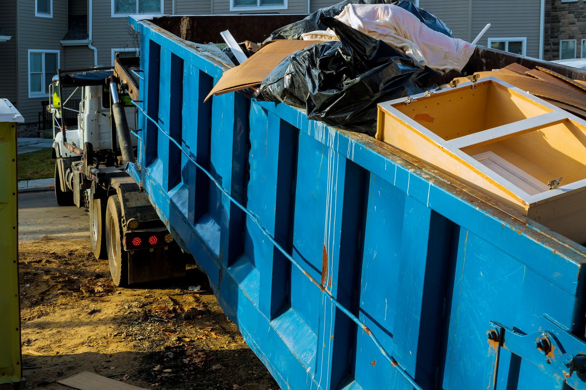 Blue dumpster truck loaded with trash parked beside an apartment building