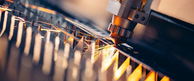 Industrial laser cutting metal with bright sparks in a factory machine.