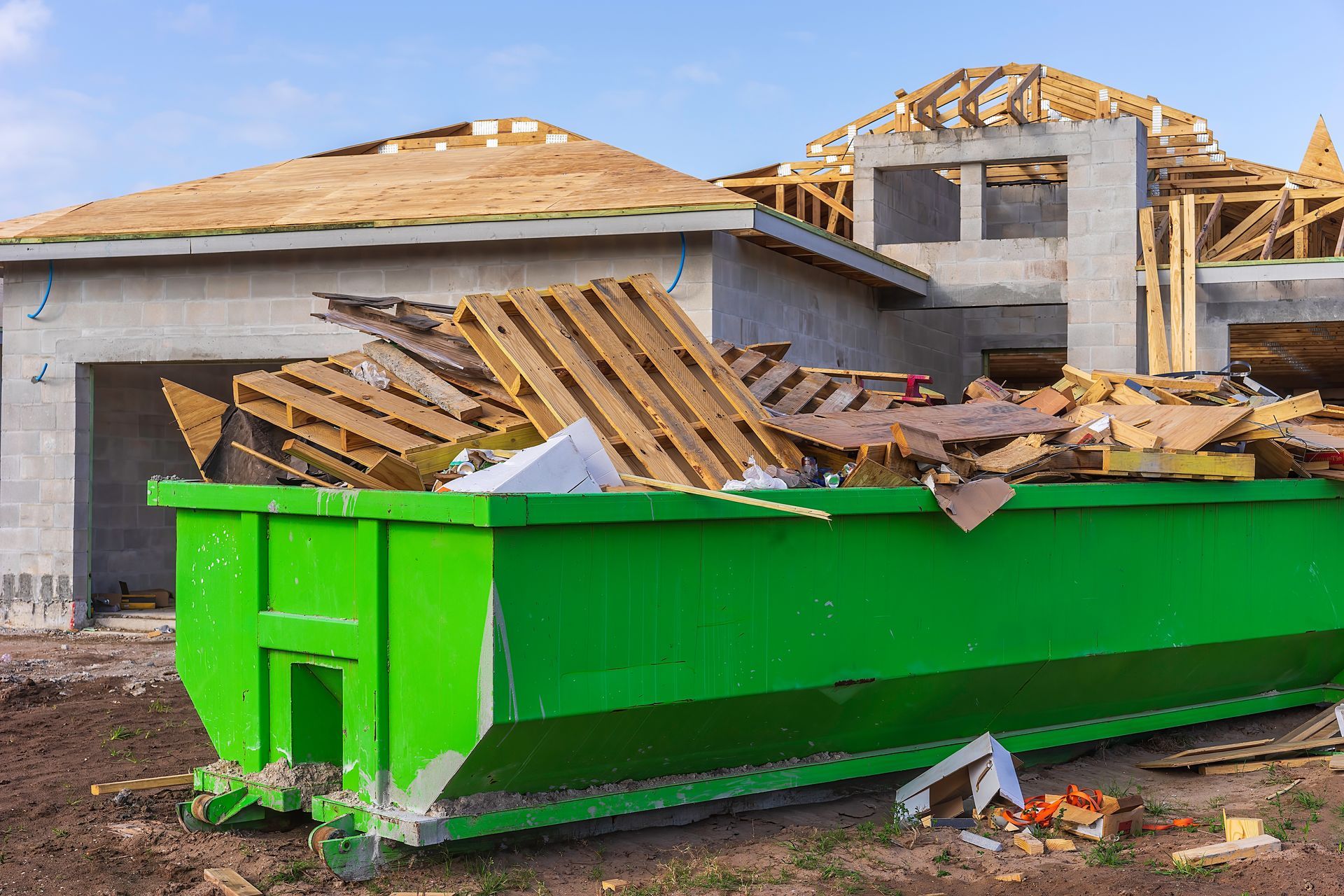 Green construction dumpster filled with debris in front of a house under renovation